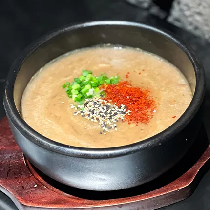 辛味やごま、ねぎが彩りよく散らされた温かいスープが器に盛られています。