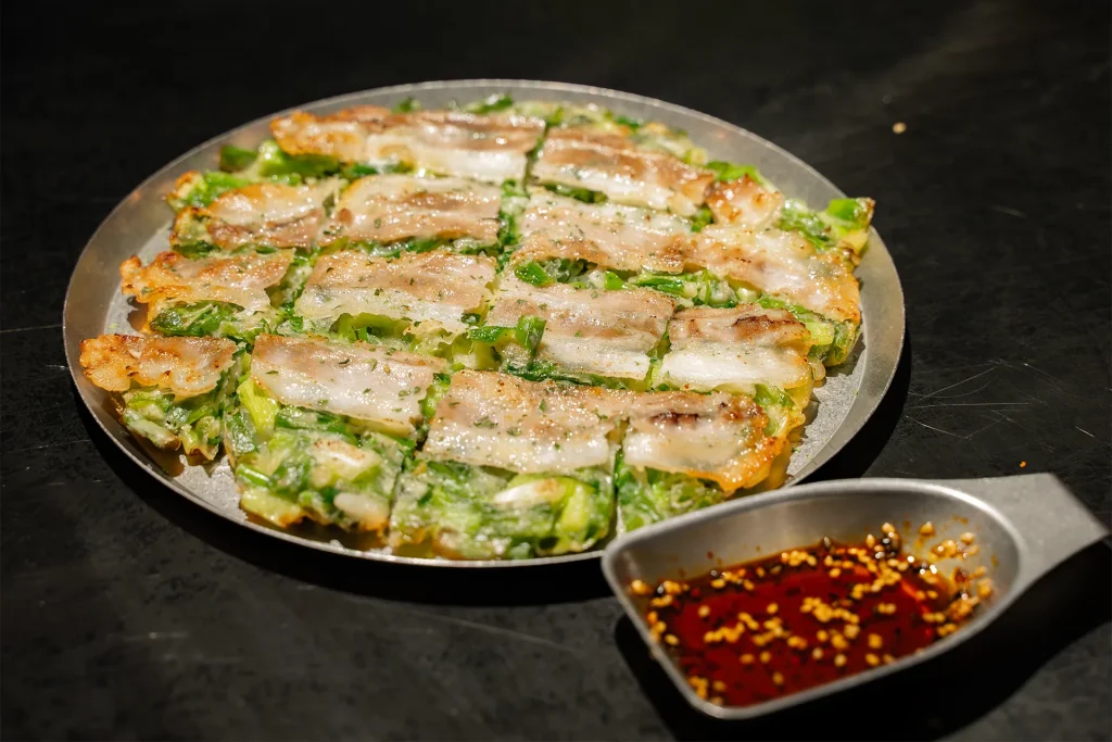 豚肉とネギがのったチヂミが香ばしく焼かれ、辛いタレと一緒に提供されています。