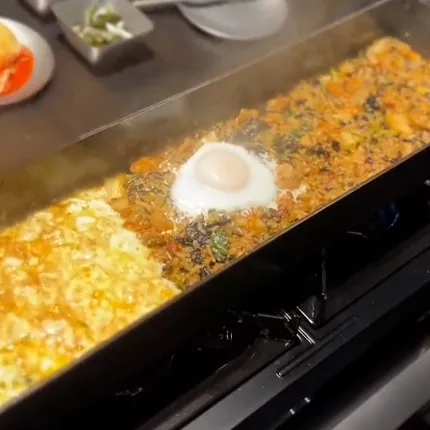 鉄板の上でキムチ炒飯と卵が同時に焼かれ、湯気が立ち上る様子です。