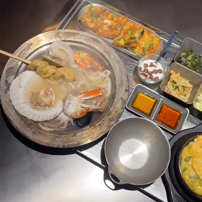 海鮮の旨味たっぷりのスープと多彩なおかずが金属トレイに並び食卓を彩っています。