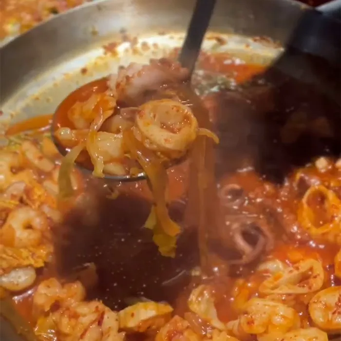 真っ赤な海鮮スープからおたまですくわれた春雨と野菜が湯気とともに映っています。