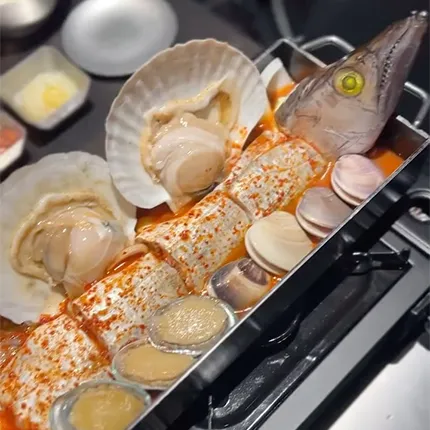 魚と貝が盛り付けられた辛い海鮮料理が鍋で加熱されている様子です。