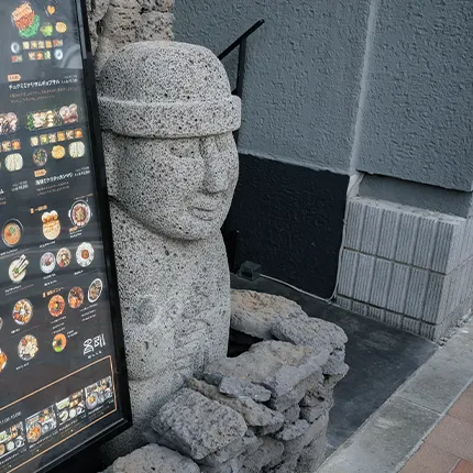 石像のトルハルバンが店のメニュー看板の横で静かに立っている様子です。