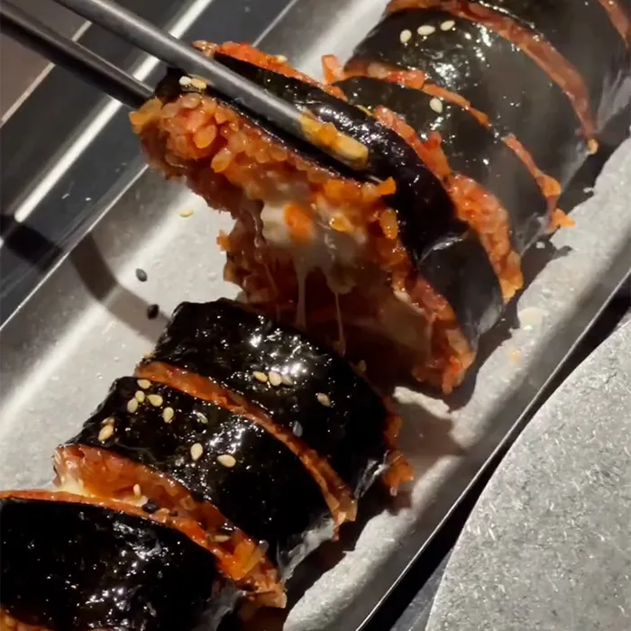 箸で持ち上げられたチーズ入りの辛いキンパがとろけ、湯気とともに美味しさを伝えます。