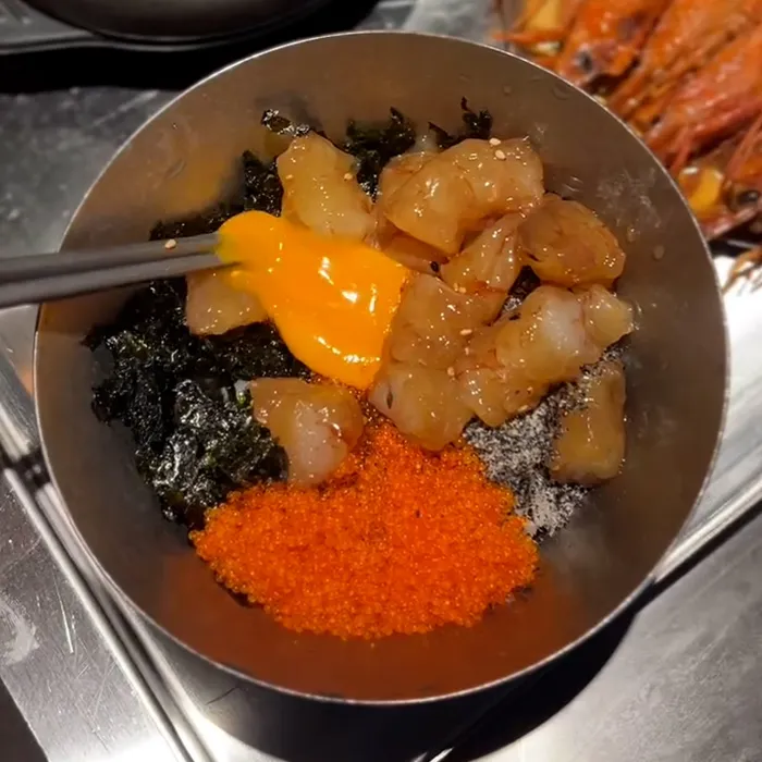 生エビや卵黄、とびこの彩りが美しい丼が混ぜる前の状態で映し出されています。